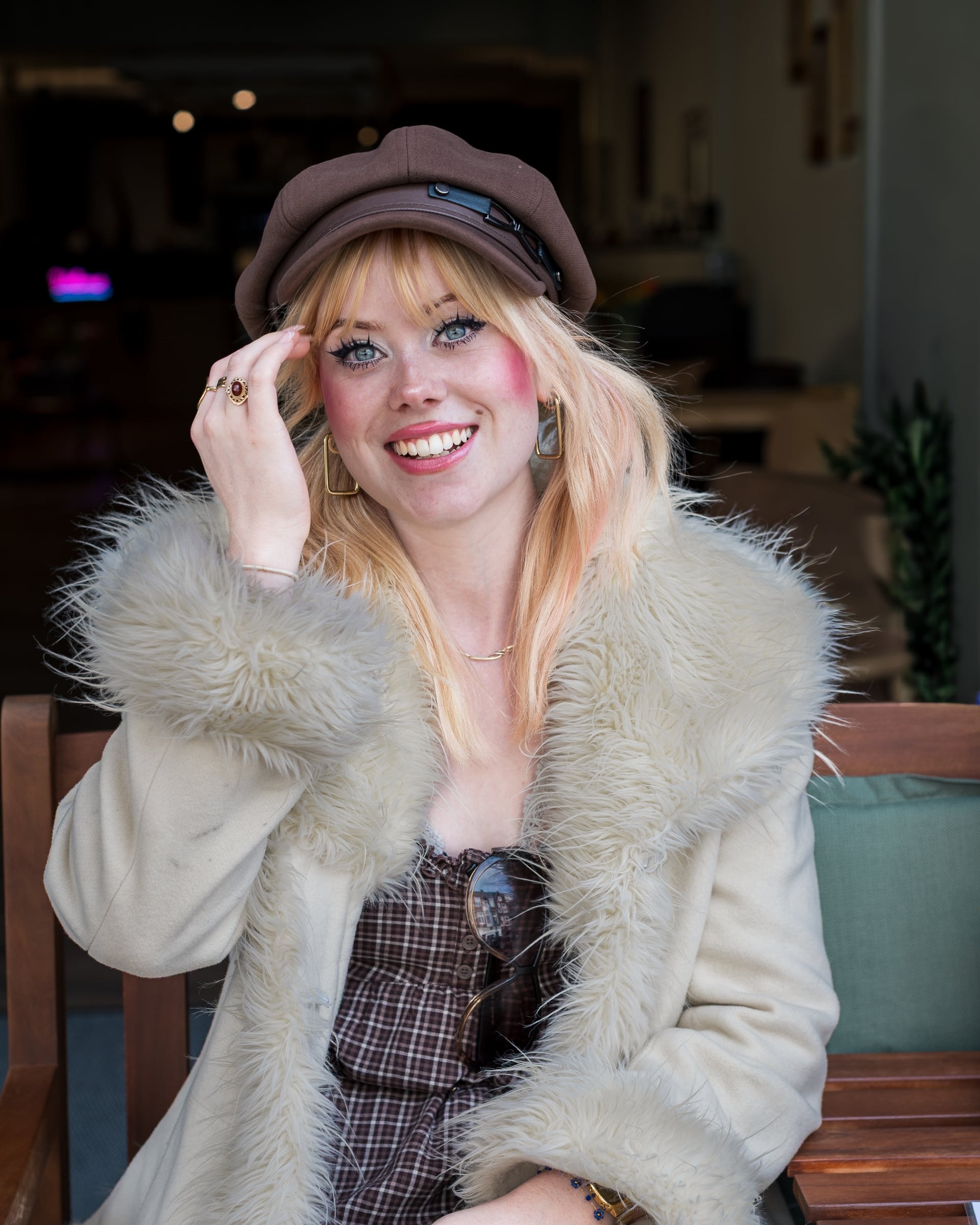 Lachend portret met bruine pet en lichte bontkraag bij een café